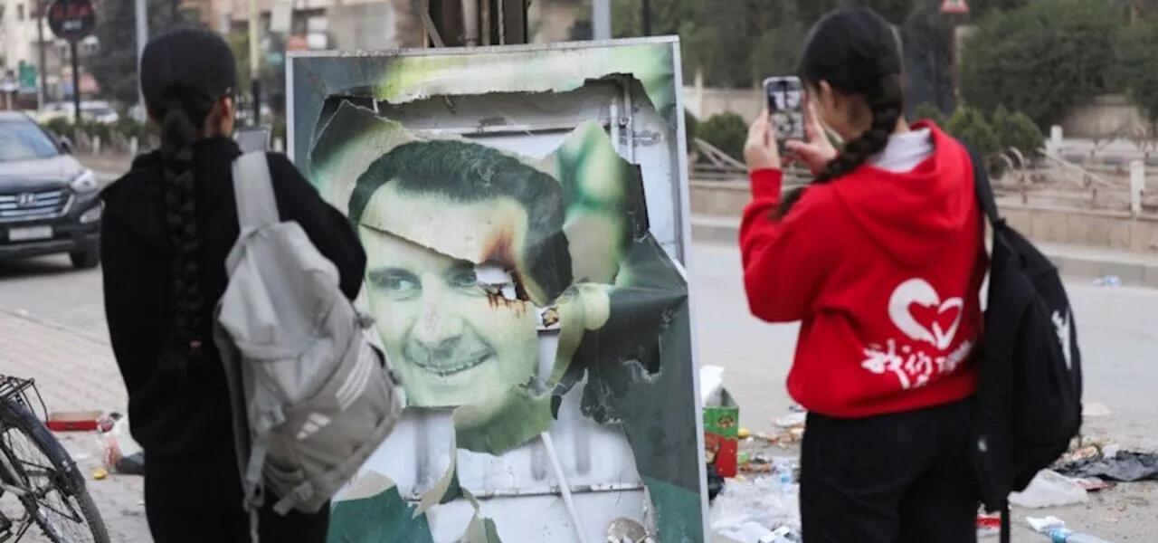 Mulheres tiram fotos de uma imagem danificada do presidente sírio Bashar al-Assad Mulheres tiram fotos de uma imagem danificada do presidente sírio Bashar al-Assad