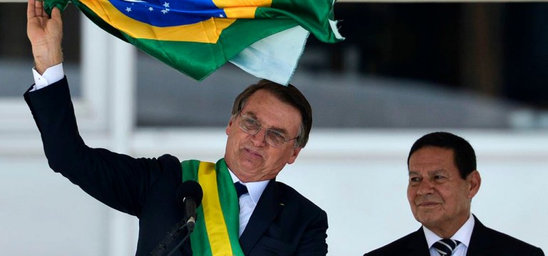 Presidente Jair Bolsonaro e o vice-presidente Hamilton Mourão exibem uma bandeira nacional durante discurso no parlatório do Palácio do Planalto.