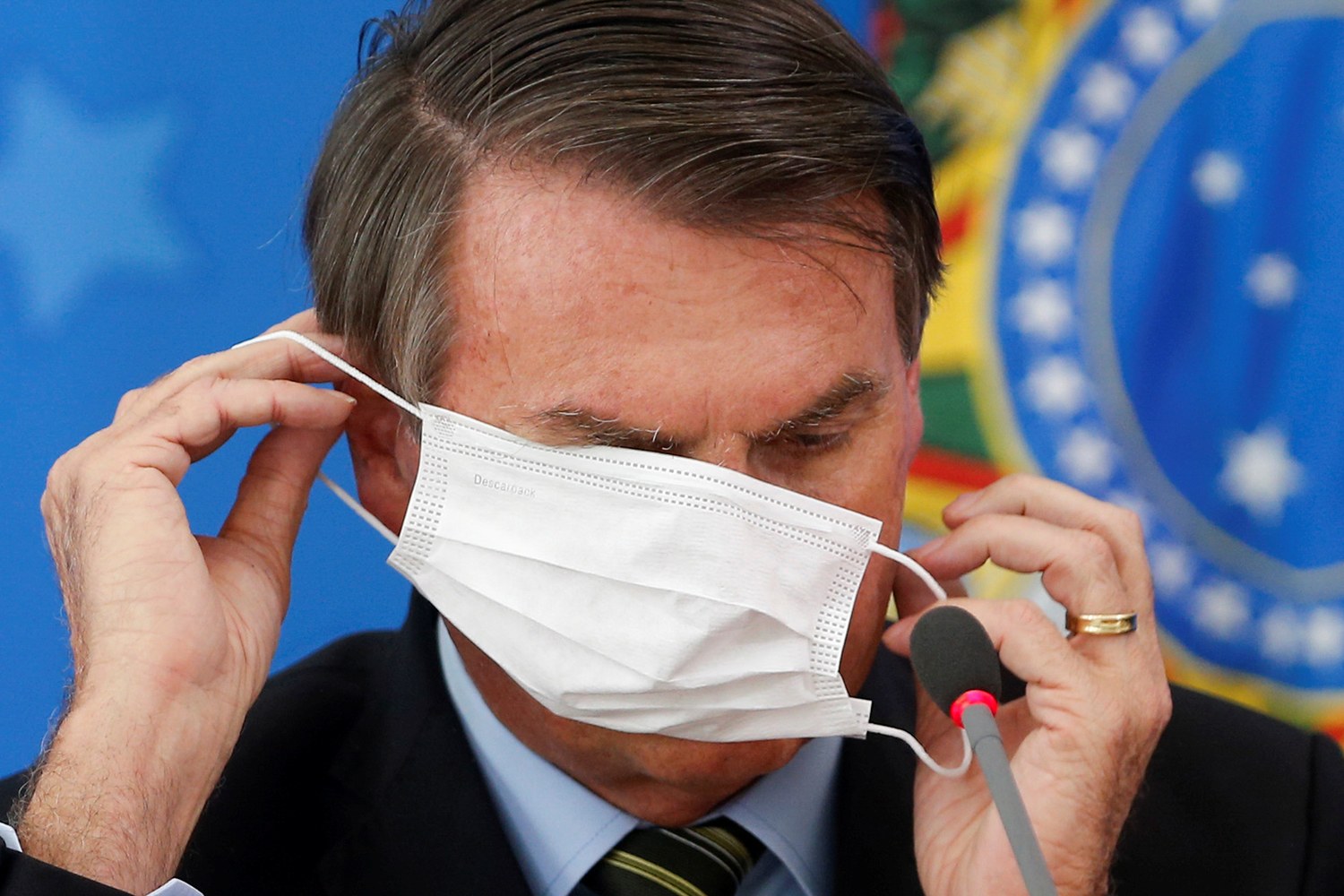 Brazil's President Jair Bolsonaro wearing a protective face masks reacts during a news conference to announce measures to curb the spread of the coronavirus disease (COVID-19) in Brasilia, Brazil March 18, 2020. REUTERS/Adriano Machado