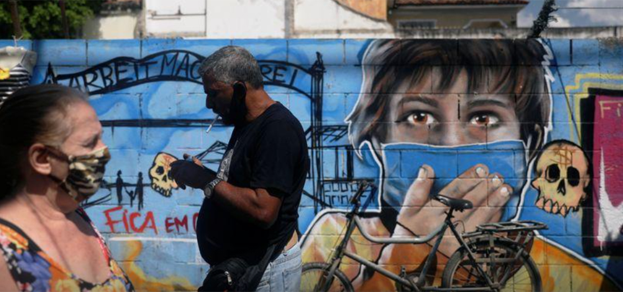 Pessoas usando máscaras de proteção passam em frente a grafite em meio à pandemia da Covid-19 no Rio de Janeiro