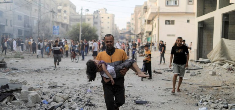 Um homem palestino carrega uma menina ferida no local dos ataques israelenses, em Khan Younis, no sul da Faixa de Gaza, 14 de outubro