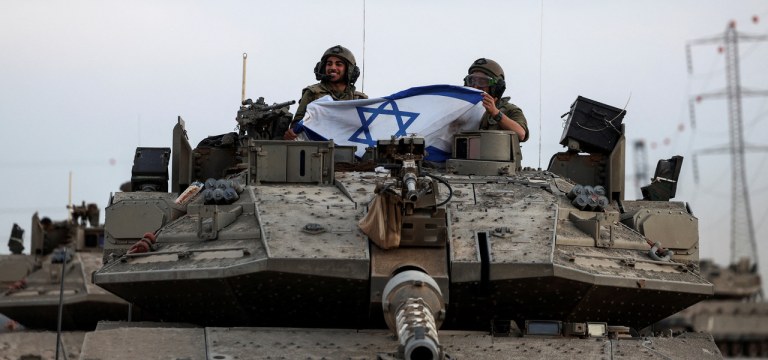 Soldados israelenses seguram bandeira israelense em um tanque perto da fronteira de Israel com a Faixa de Gaza