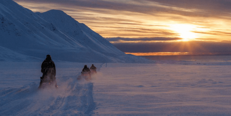 Cientistas dirigem seus veículos para neve cruzando o Ártico em direção a Kongsfjord durante o pôr do sol perto de Ny-Alesund, Svalbard, Noruega, 10 de abril de 2023