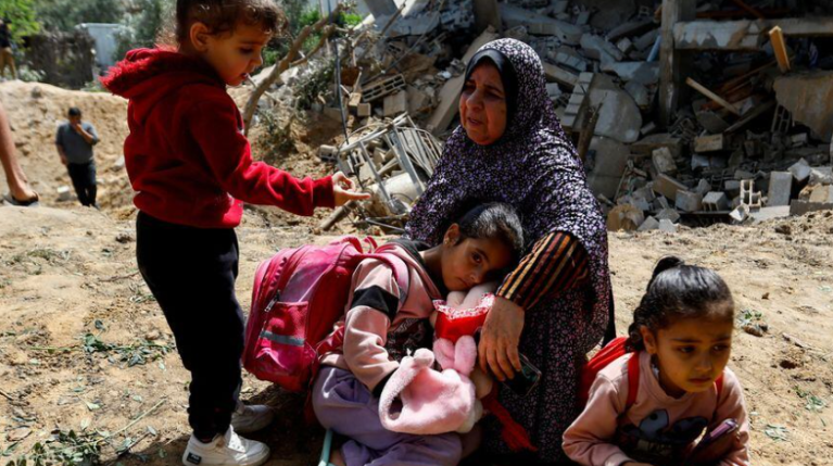 Uma mulher palestina, Fatima Bashir, e suas netas sentam-se ao lado dos restos de sua casa, que foi destruída em ataques aéreos israelenses, na cidade de Deir al-Balah, no centro da Faixa de Gaza, 12 de maio de 2023