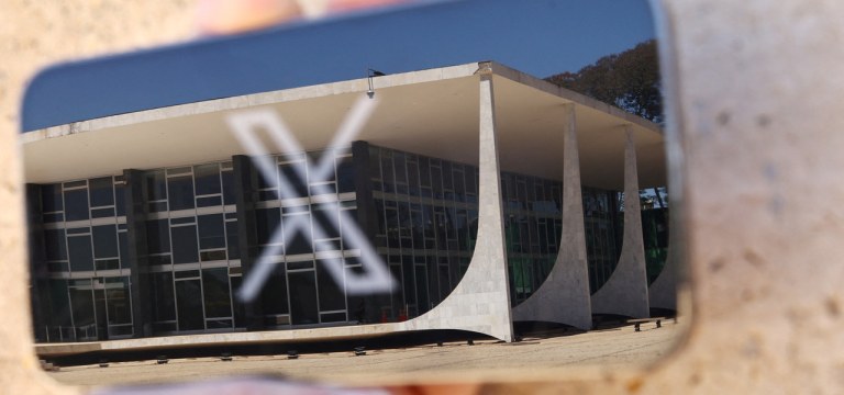 Logo da rede social X exibida em celular com reflexo do prédio do STF em Brasília