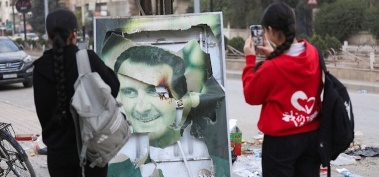 Mulheres tiram fotos de uma imagem danificada do presidente sírio Bashar al-Assad