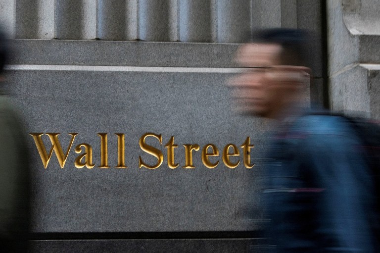 Homem passa em frente a sinalização de Wall Street, em Nova York, EUA - 29/12/2023