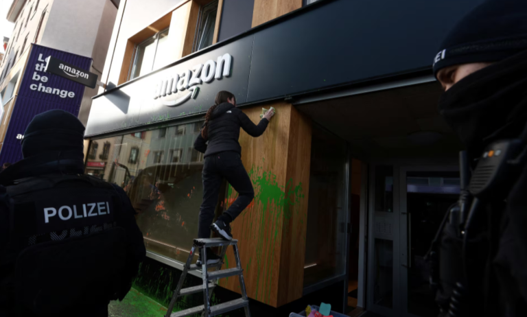 A polícia suíça fica em frente a um espaço da Amazon enquanto uma mulher limpa a vitrine depois que ativistas pintaram sua fachada com spray durante um protesto no dia de abertura da 55ª reunião anual do Fórum Econômico Mundial (WEF) em Davos, Suíça , 20 de janeiro de 2025