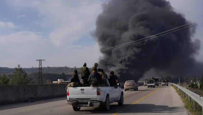 Fumaça sobe enquanto membros das novas forças regulares sírias viajam em um veículo enquanto lutam contra uma insurgência incipiente de combatentes aliados ao líder deposto Bashar al-Assad, em Latakia, Síria, 7 de março de 2025