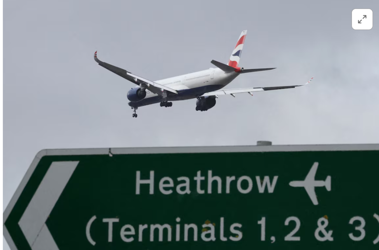 Um avião de passageiros da British Airways sobrevoa uma placa de sinalização rodoviária enquanto faz sua aproximação para pouso no Aeroporto de Heathrow, no oeste de Londres, Grã-Bretanha