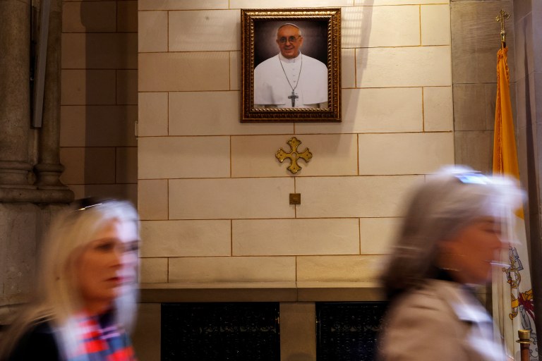 Mulheres passam por um retrato do Papa Francisco - 25/02/2025
