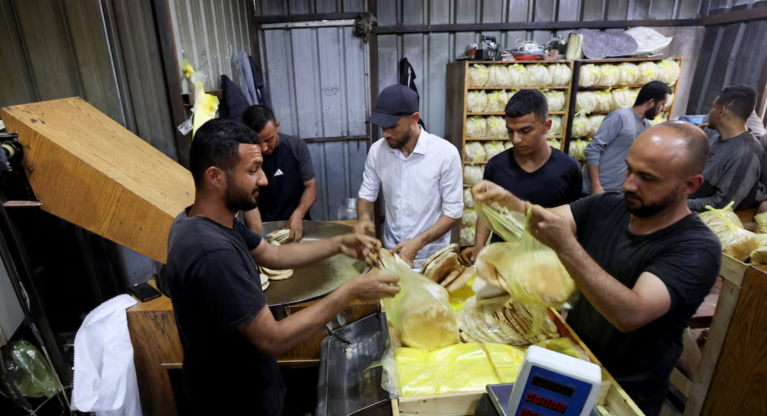 Trabalhadores palestinos embalam pão em uma padaria que voltou a operar após ser fechada devido à escassez de farinha, em Deir Al-Balah, no centro da Faixa de Gaza, em 22 de maio de 2025