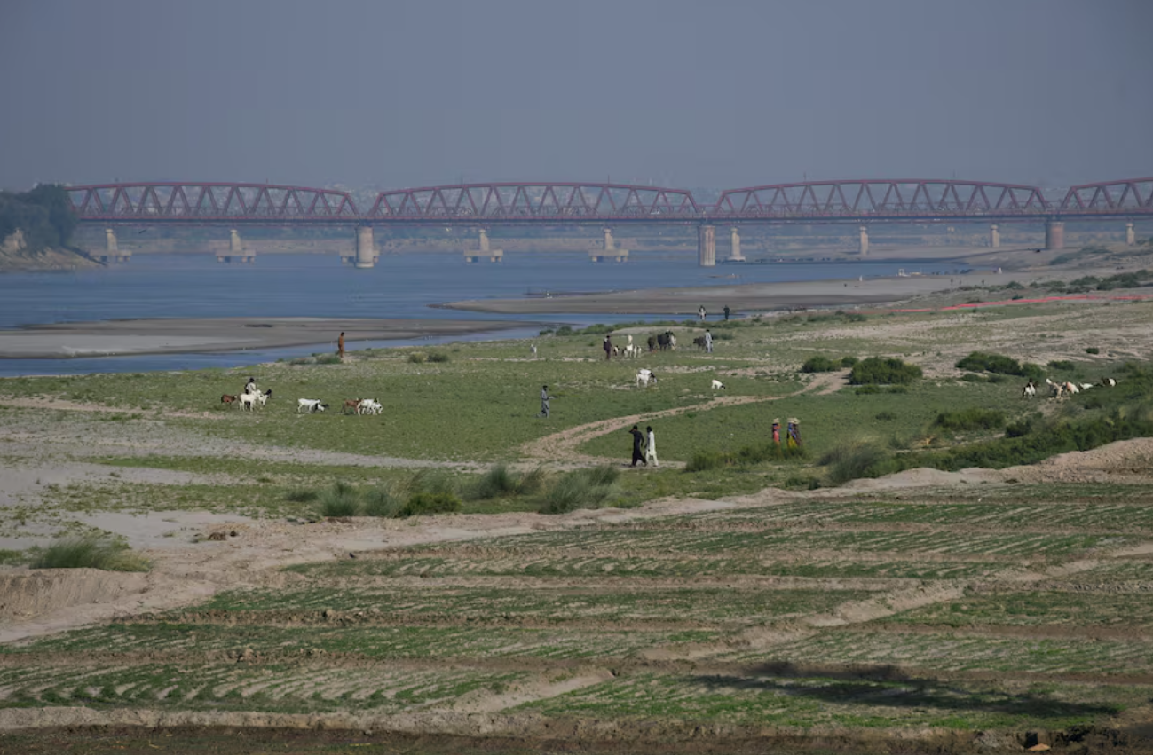 Pessoas caminham ao lado de uma terra cultivada no leito seco do rio Indo, em Hyderabad, Paquistão, em 25 de abril de 2025