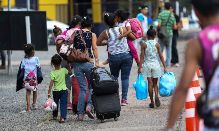 Mulheres e crianças em mudança carregam malas e sacolas