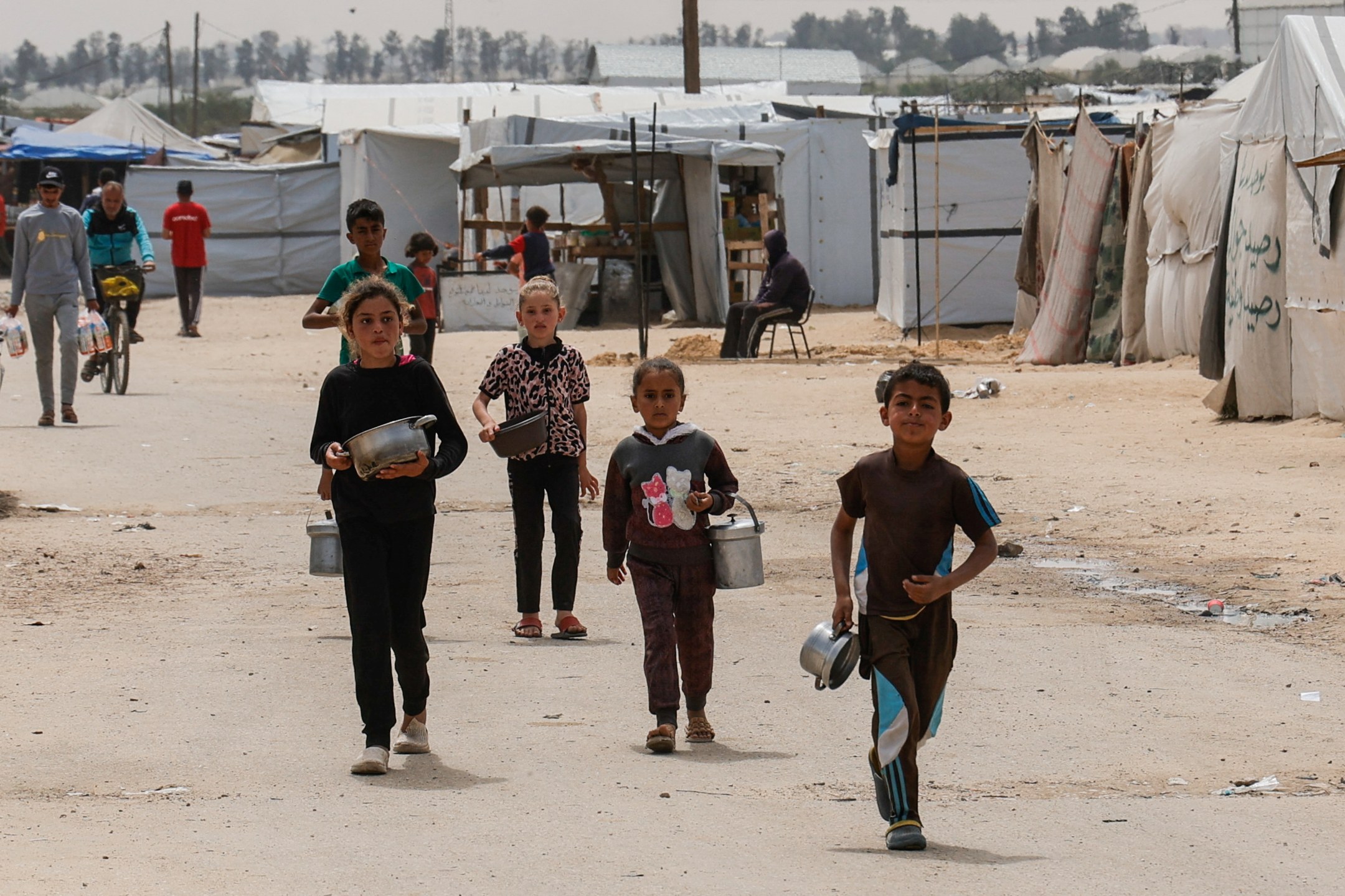 Crianças caminham enquanto palestinos esperam para receber comida preparada por uma cozinha comunitária, em Khan Younis, no sul da Faixa de Gaza - 06/04/2025