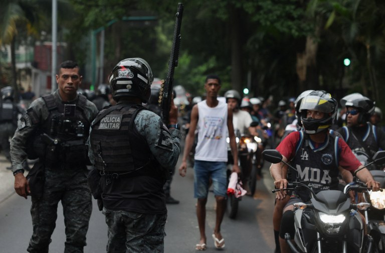 Policial segura arma enquanto moradores dos complexos do Alemão e da Penha protestam do lado de fora da sede do governo do estado do Rio de Janeiro, após a chacina policial que matou ao menos 121 pessoas - 29/10/2025