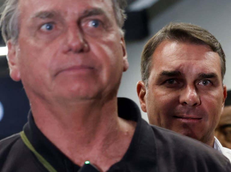 O senador Flávio Bolsonaro observa o pai, o ex-presidente Jair Bolsonaro, no Aeroporto Internacional de Brasília - 25/11/2024