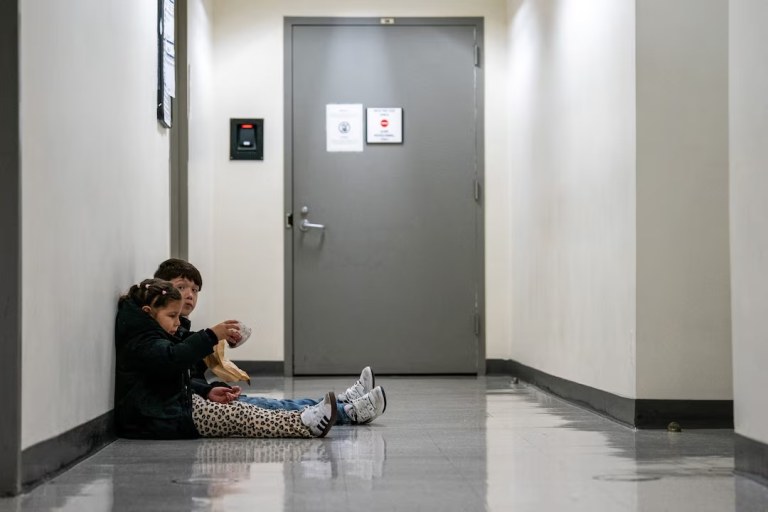 Duas crianças sentam-se no corredor enquanto seus pais participam de uma audiência de imigração no tribunal de imigração dos Estados Unidos, em Manhattan, na cidade de Nova York, em 24 de outubro de 2025