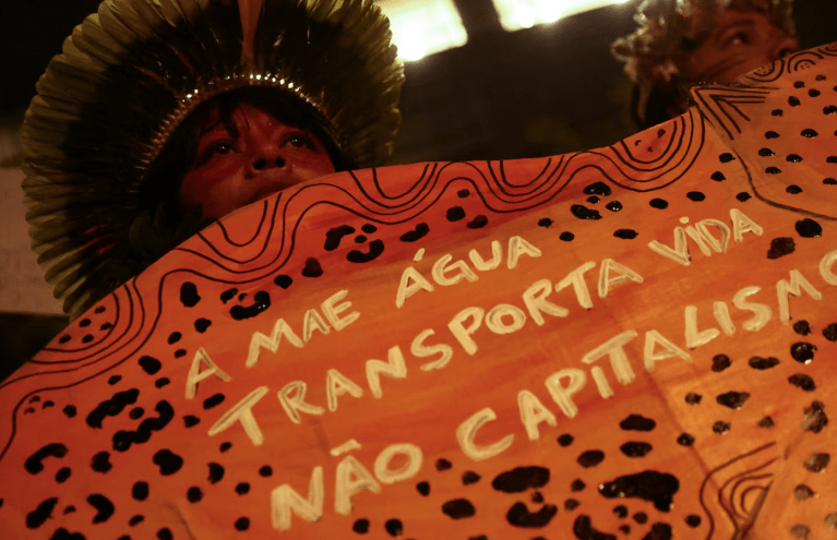 Manifestante exibe um cartaz durante uma manifestação em frente aos escritórios da Cargill, em apoio a grupos indígenas que vêm bloqueando o tráfego de caminhões há vários dias na entrada do terminal da Cargill em Santarém, no norte do Brasil, em protesto contra os planos de dragar o rio Tapajós e aumentar o transporte de grãos, como soja e milho, destinados aos mercados de exportação, em São Paulo, 20 de fevereiro de 2026.