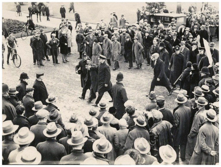 Polícia detém manifestante durante ato do Movimento dos Trabalhadores Desempregados (Unemployed Workers’ Movement) diante do Parlamento da Nova Zelândia, em 1931, em meio à crise social provocada pela Grande Depressão. Foto: Archives New Zealand — Unemployed Workers’ Movement protest, Wellington, 1931 (ADMO 21007 W5985).