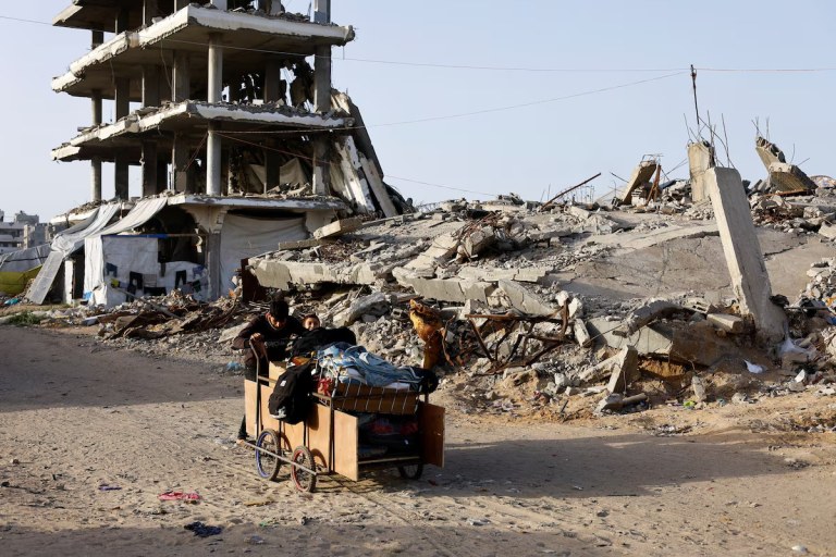 Palestinos empurram um carrinho pelo entulho de prédios residenciais destruídos em Gaza, 17 de fevereiro de 2026