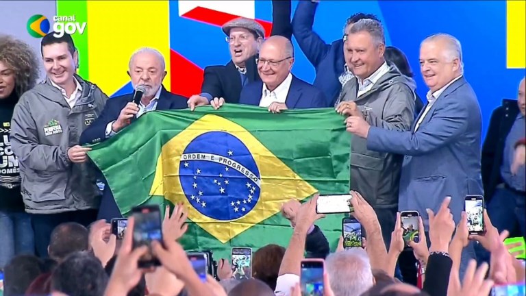 O presidente Luiz Inácio Lula da Silva, com o vice-presidente Geraldo Alckmin, seguram uma bandeira do Brasil, com ministros e outras figuras políticas, em Osasco, SP - 25/07/2025