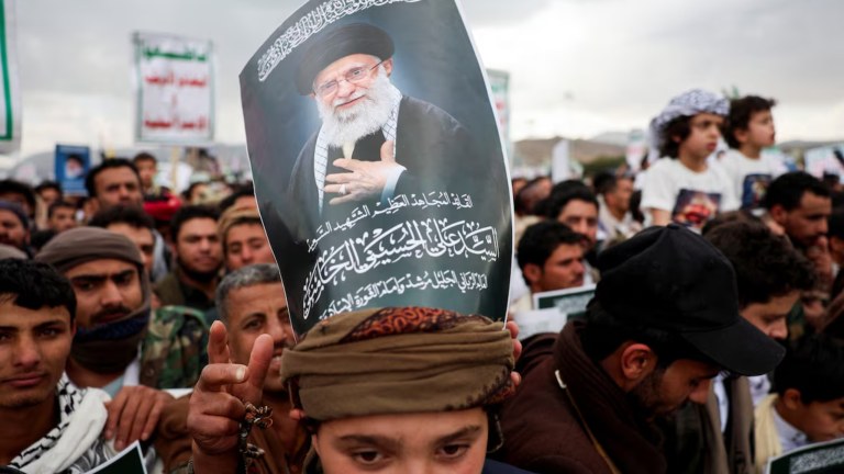 Um manifestante com um cartaz sobre a cabeça exibindo a imagem de Ali Khamenei, participa de uma manifestação com apoiadores houthis em solidariedade ao Irã e ao Líbano